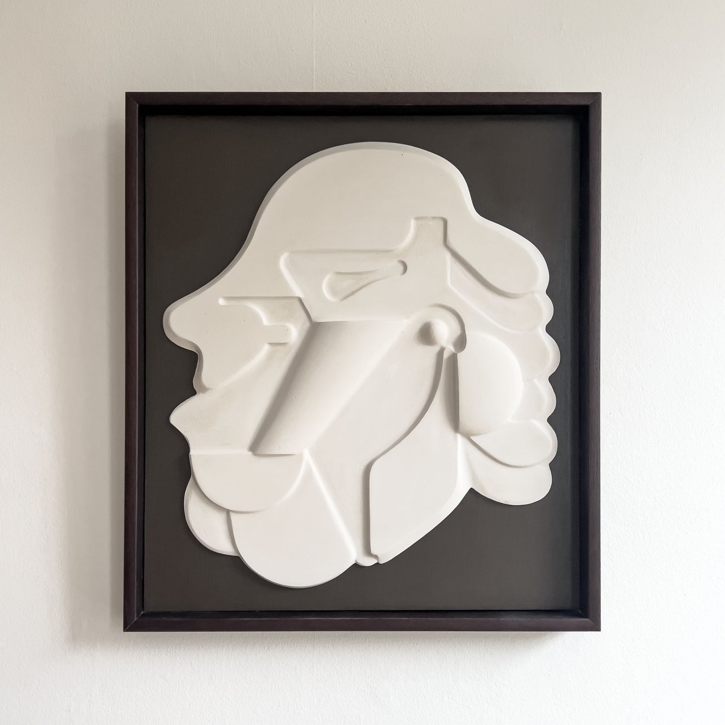 Mask 1, a relief wall sculpture artwork photographed against a white wall. The relief is framed in mahogany stain and brown backboard.