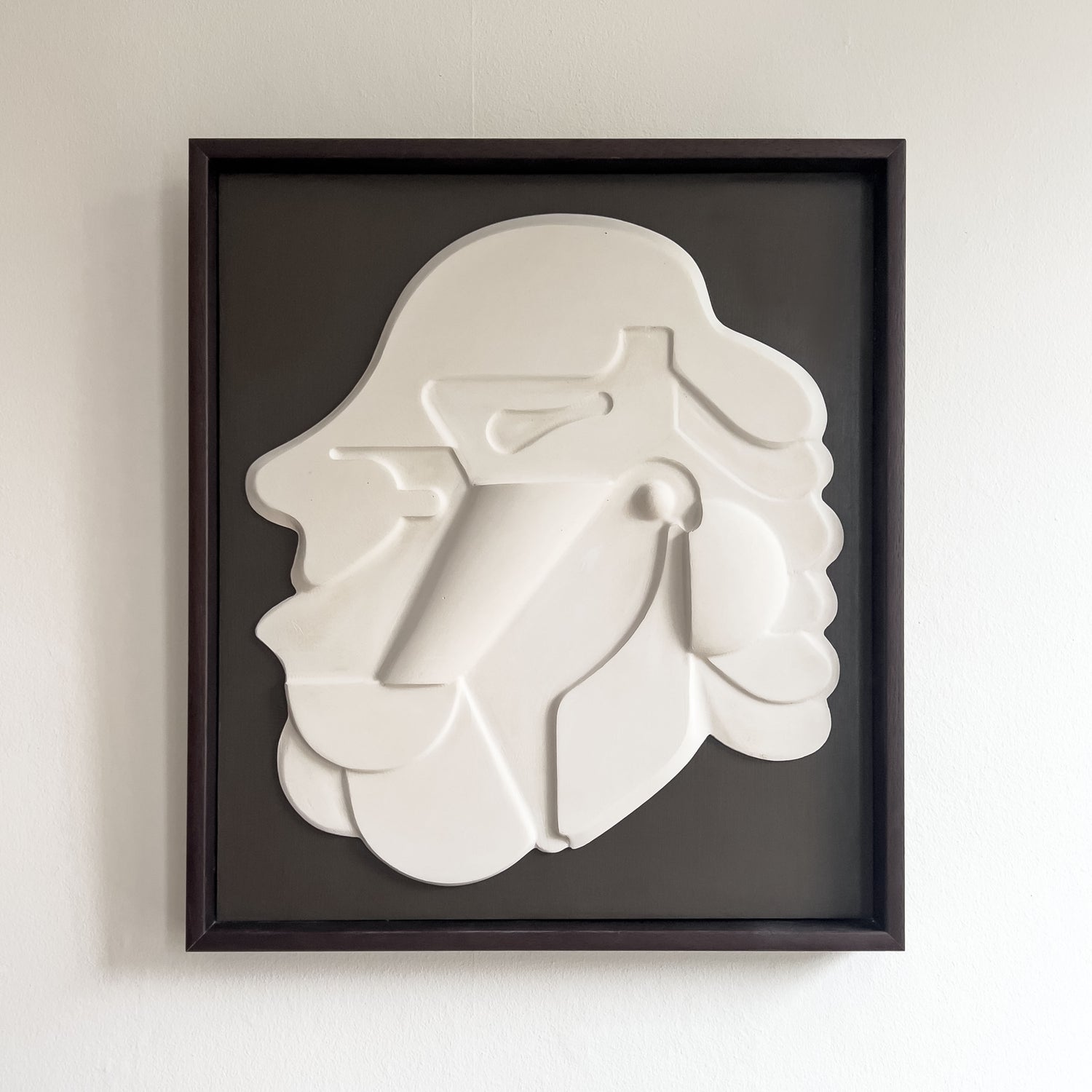 Mask 1, a relief wall sculpture artwork photographed against a white wall. The relief is framed in mahogany stain and brown backboard.