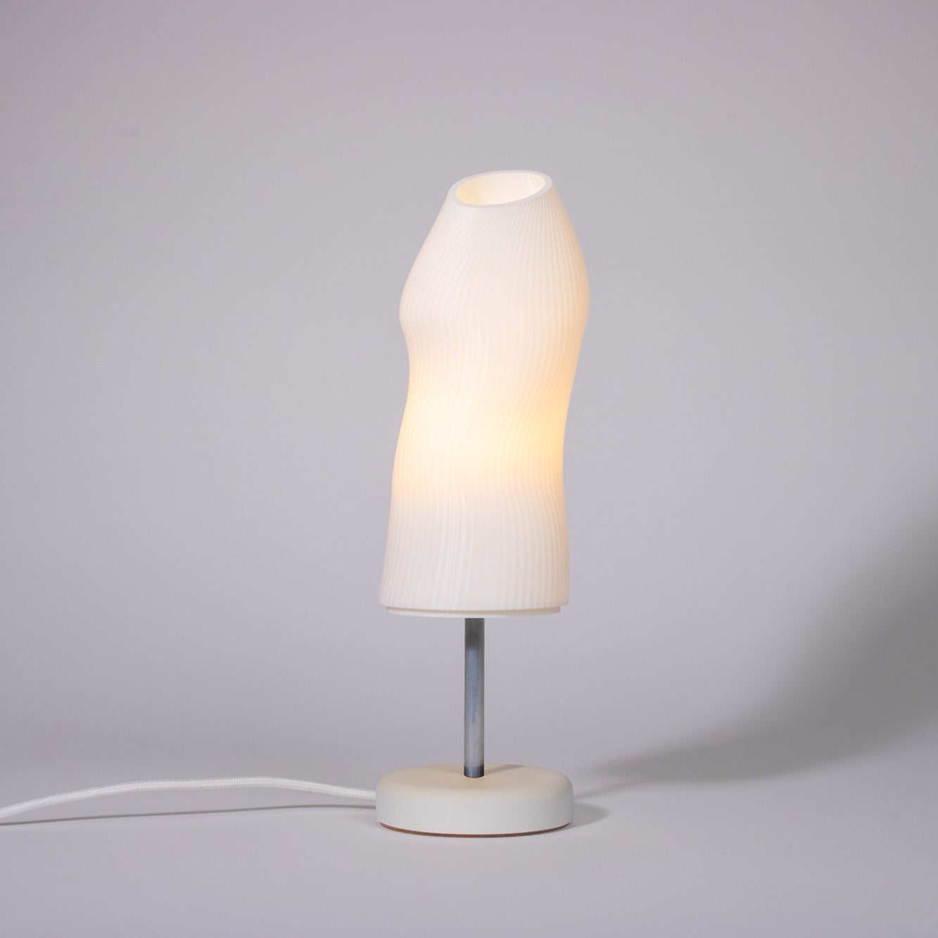 Ora Premium white sculptural table lamp with white plaster base and chrome rod photographed against a white background