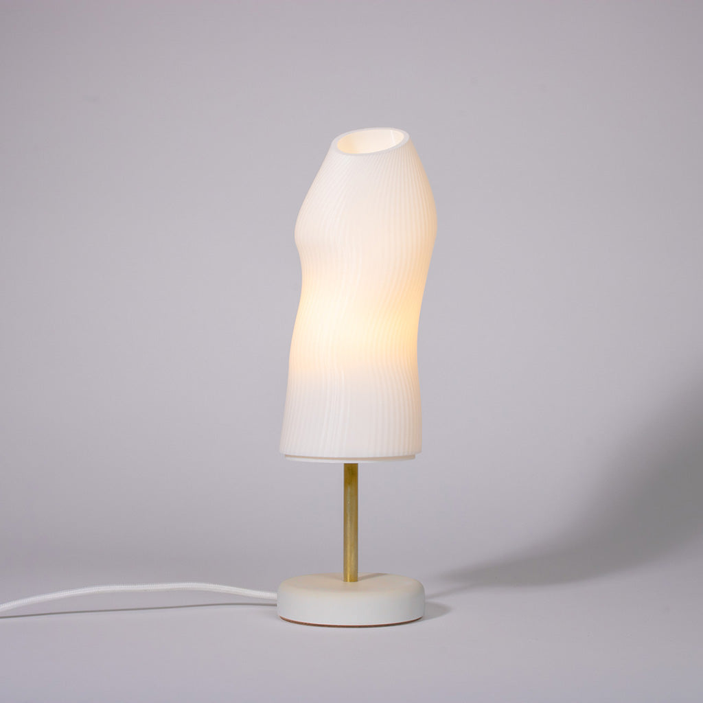 Ora Premium white sculptural table lamp with a white plaster base and a brass rod photographed against a white background