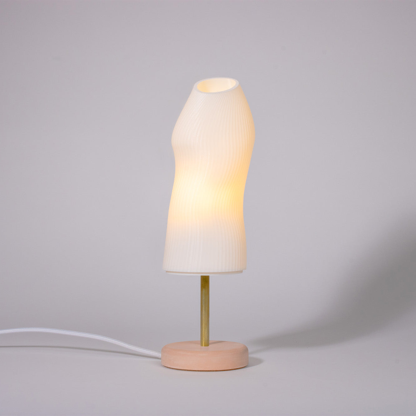 Ora Premium white sculptural table lamp with red plaster base and brass rod photographed against a white background