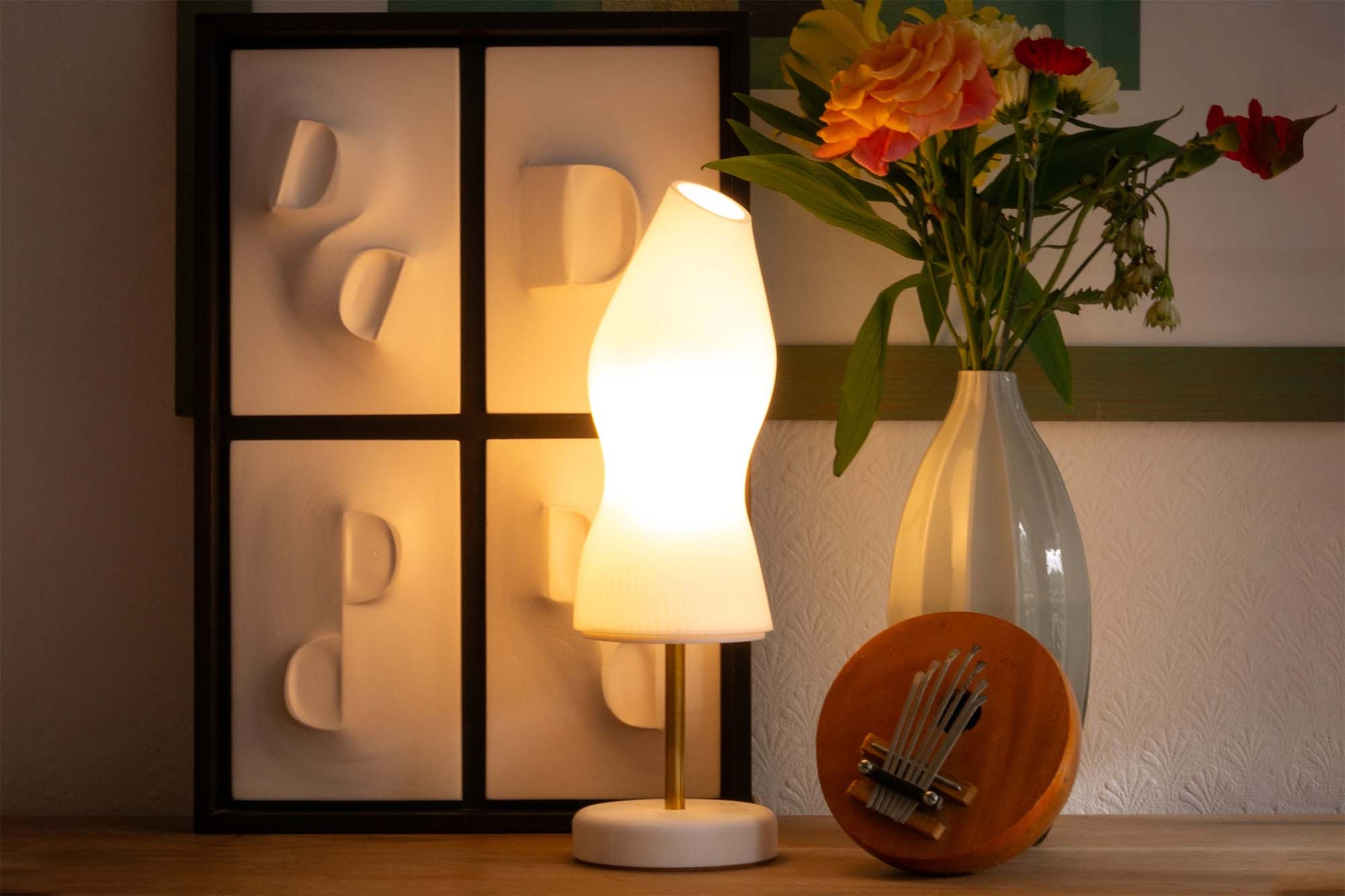 Ora Premium table lamp styled against a white sculpture with flowers and a music instrument