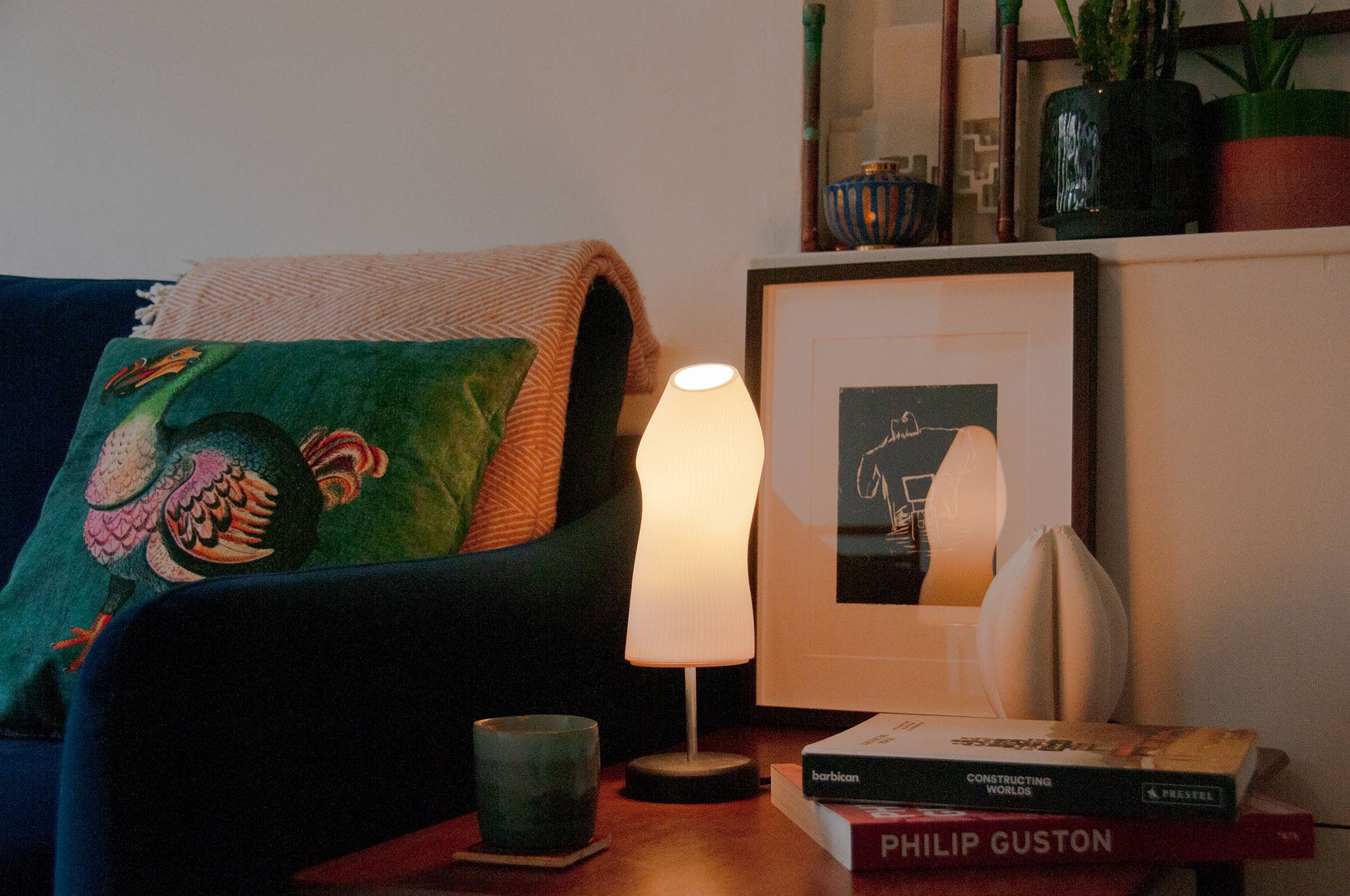 Ora sculptural table lamp with a black base shining a dark living room on a wooden desk