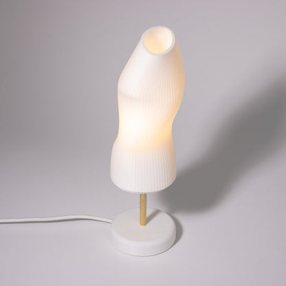 Ora white sculptural table lamp with a white base and a brass rod photographed against a white background