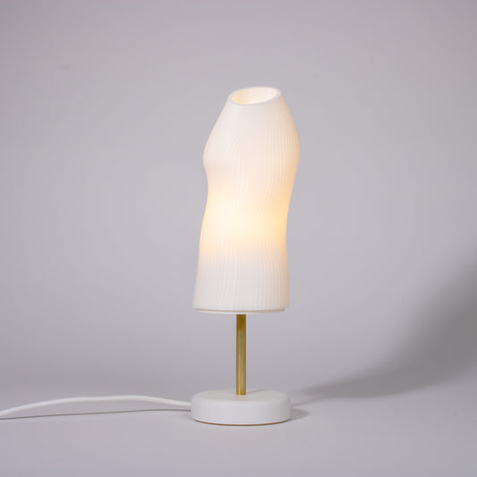 Ora white sculptural table lamp with white base and brass rod photographed against a white background