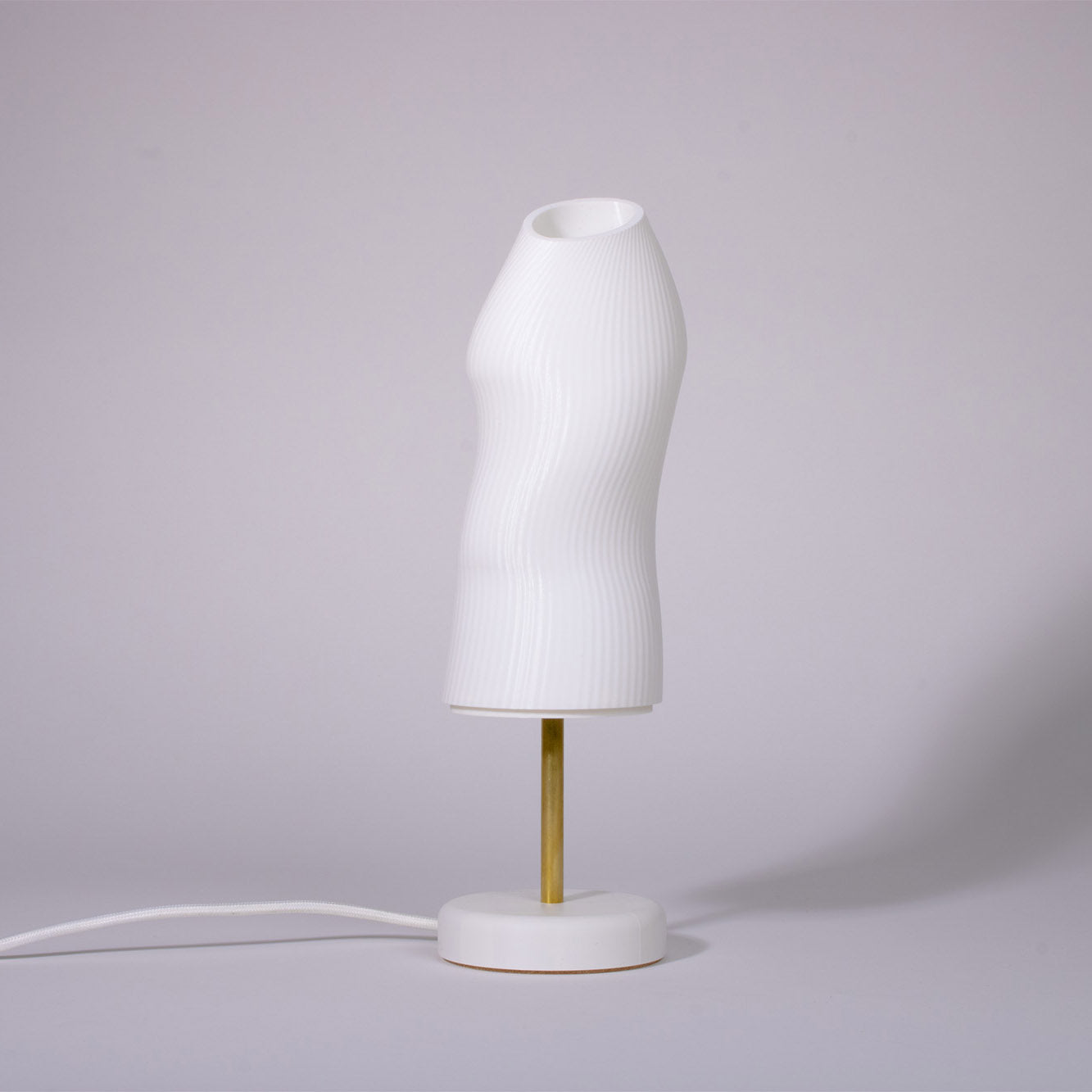 Ora white sculptural table lamp with a white base and a brass rod photographed against a white background